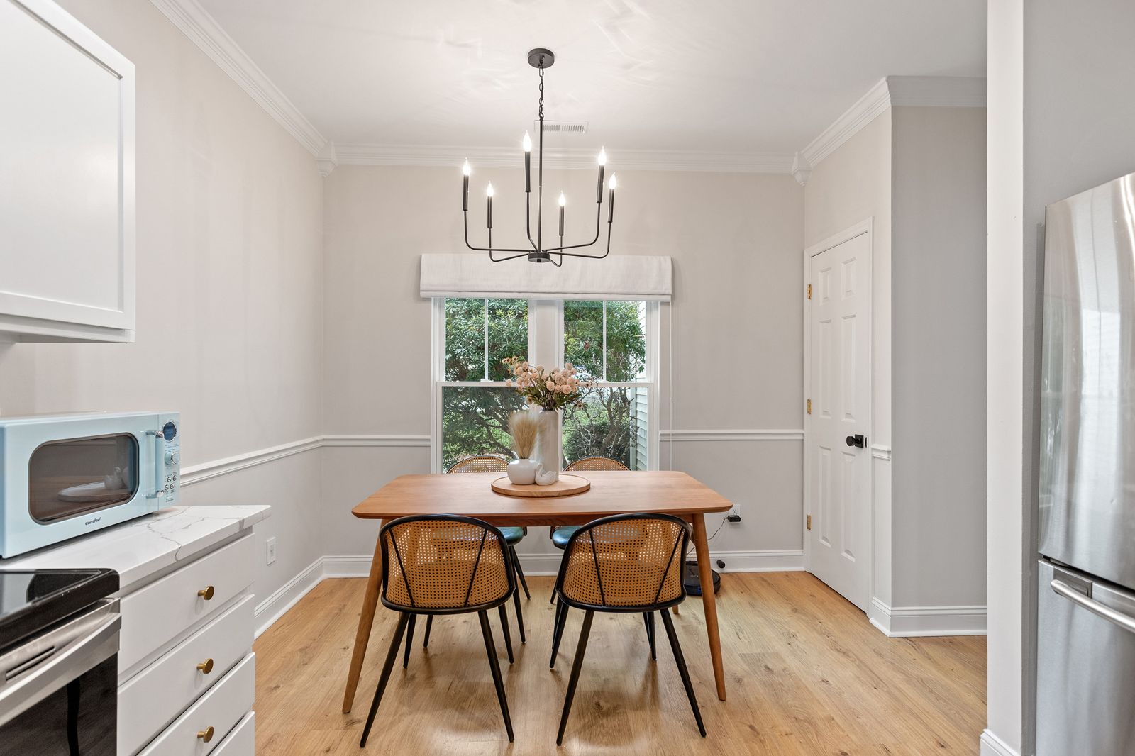 Dining area with a mid-century wood table, cane chairs and a black chandelier